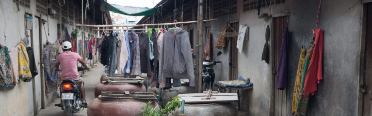 Motorradfahrer in einer sehr engen und mit Kleidern und Töpfen verstellten Strasse