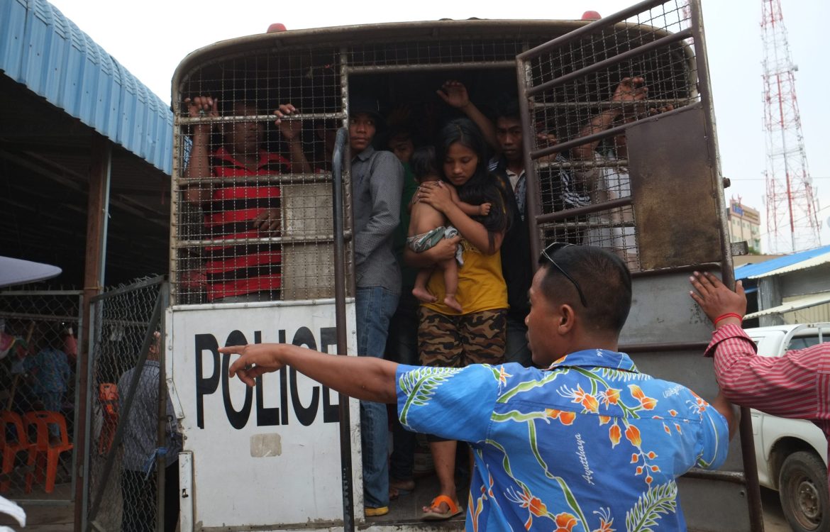 Migrant workers are crammed into a van by the Thai police, including a young woman with a baby.