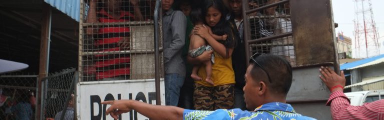 Des migrant·e·s sont entassés dans un fourgon de police par des policiers thaïlandais, dont une jeune femme avec un bébé.