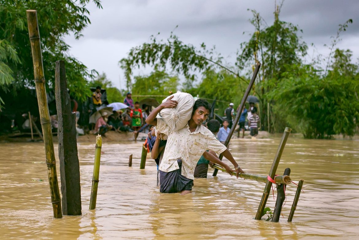Mann in Rohingya-Camp trägt Hilfsgüter durch die Fluten..